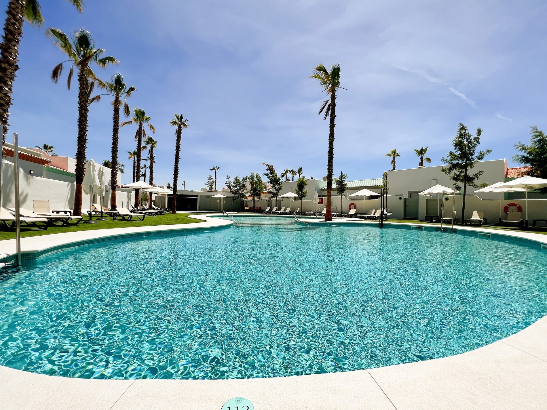 una piscina rodeada de palmeras y mesas y sillas