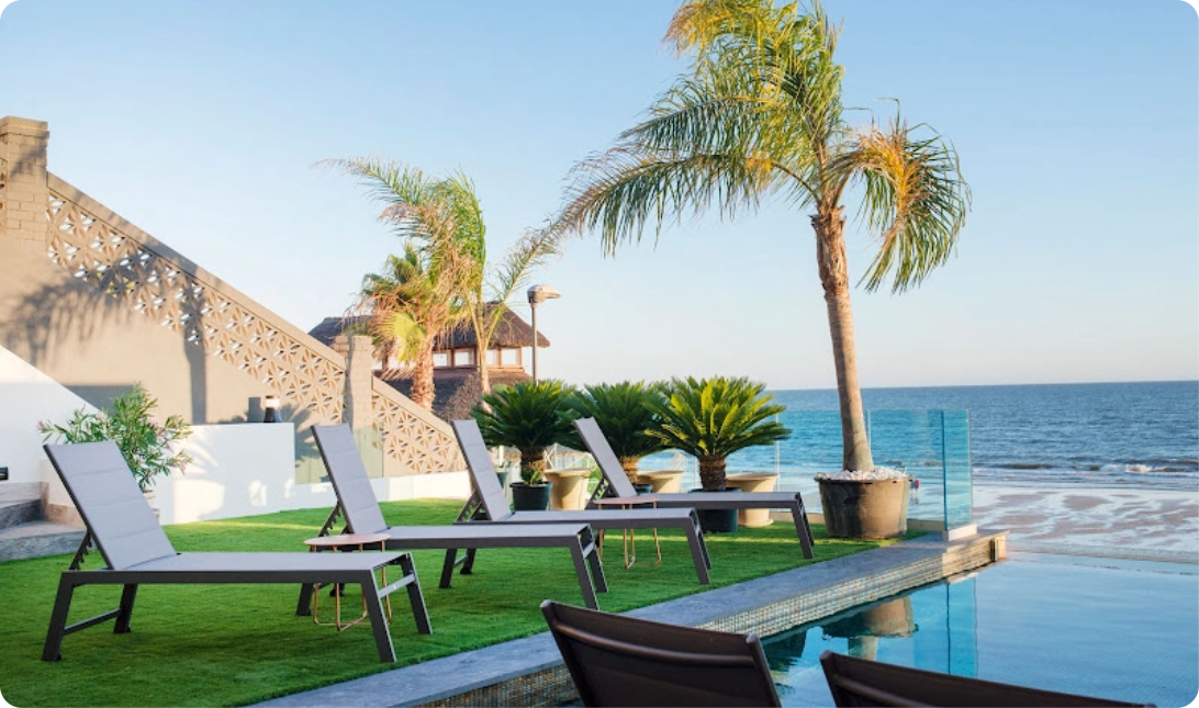 una piscina rodeada de sillas y palmeras con vistas al océano