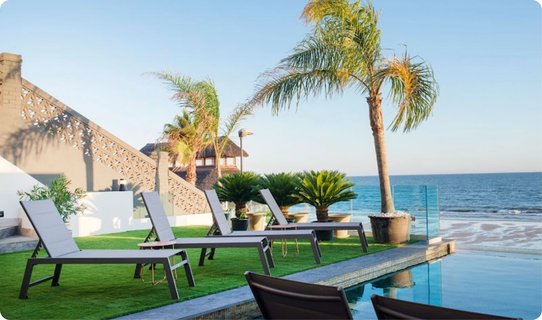 a swimming pool surrounded by chairs and palm trees overlooking the ocean