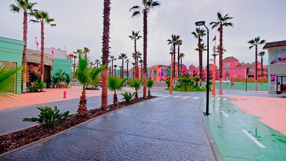 a row of palm trees are lined up in front of a pink building