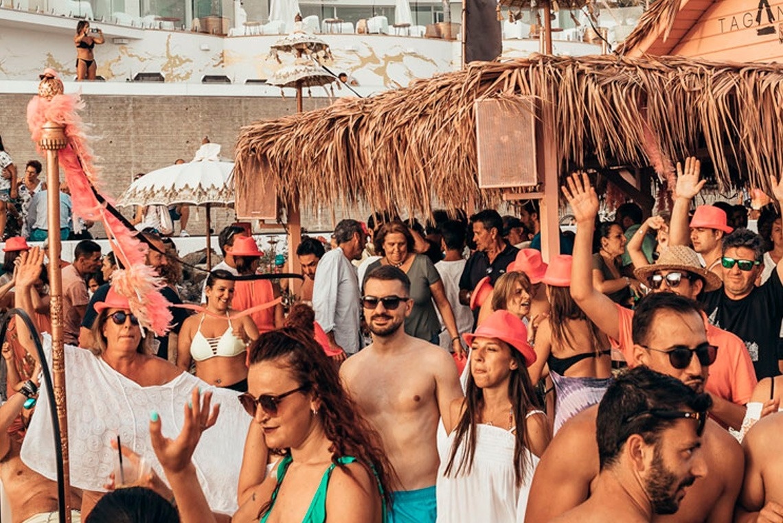 a crowd of people are gathered in front of a thatched hut that says tag on it