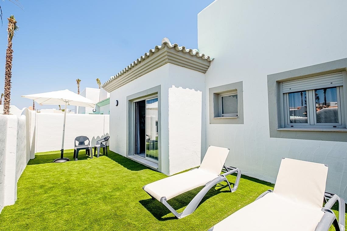 un patio con sillas y sombrillas frente a una casa blanca