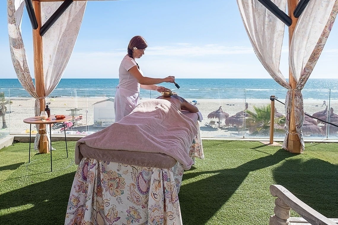 una mujer está dando un masaje a una mujer en una cama con vista al océano