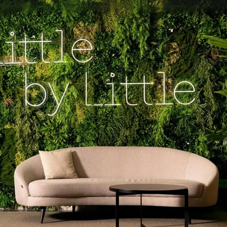 ein Wohnzimmer mit einer Couch und einem Tisch und einer Wand mit der Aufschrift " little by little "