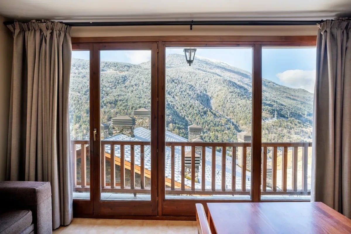 ein Wohnzimmer mit einem Tisch und einem Balkon mit Blick auf die Berge
