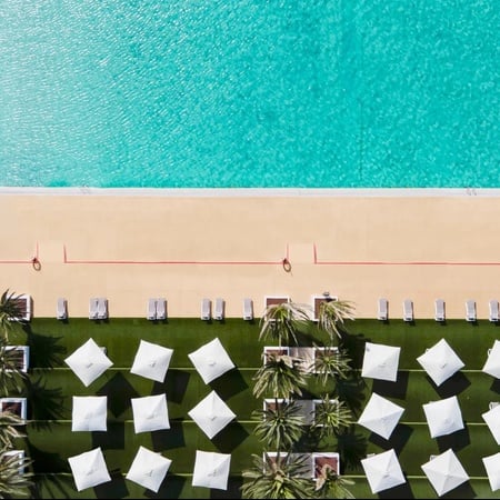 eine Luftaufnahme eines Pools mit weißen Sonnenschirmen und Stühlen