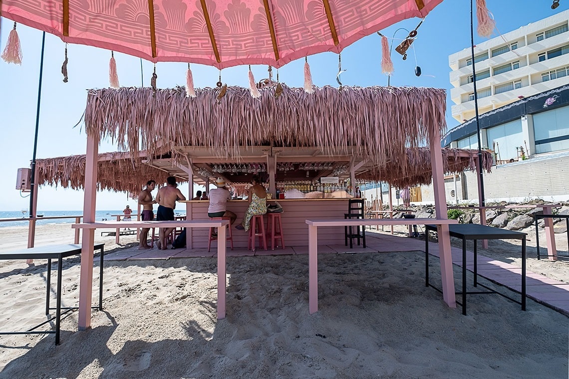 un bar rosa en la playa con un paraguas rosa