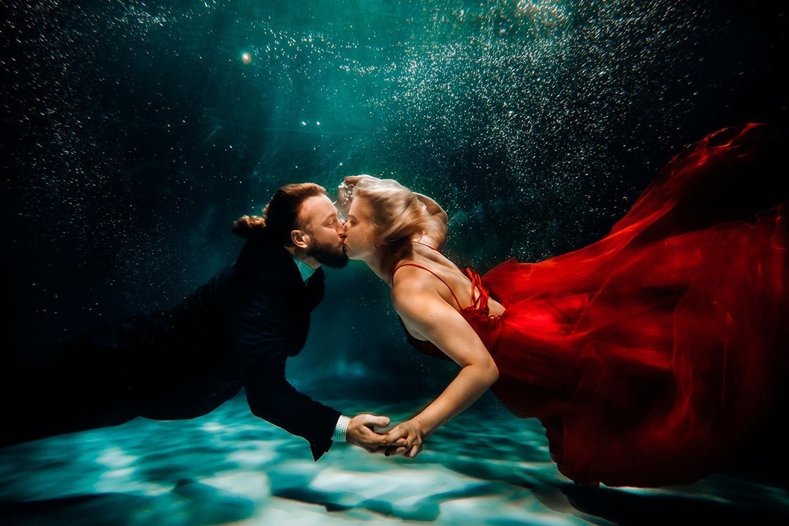 a man and a woman are kissing underwater and the woman is wearing a red dress