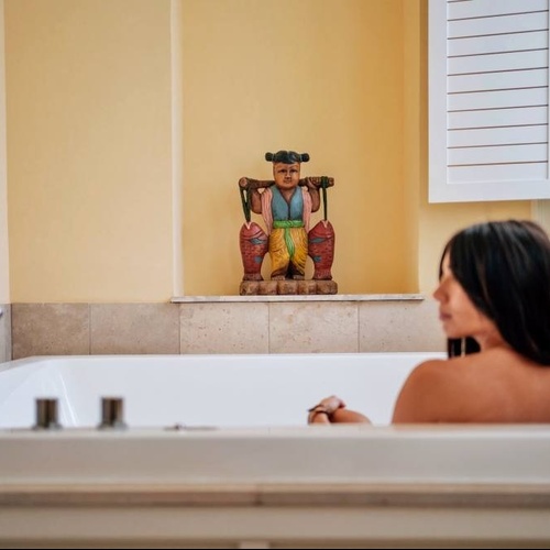 une femme se baigne dans une baignoire avec une statue en bois au mur