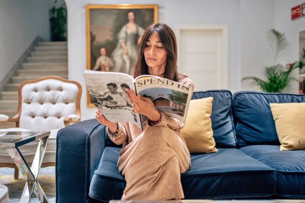une femme est assise sur un canapé en train de lire une revue