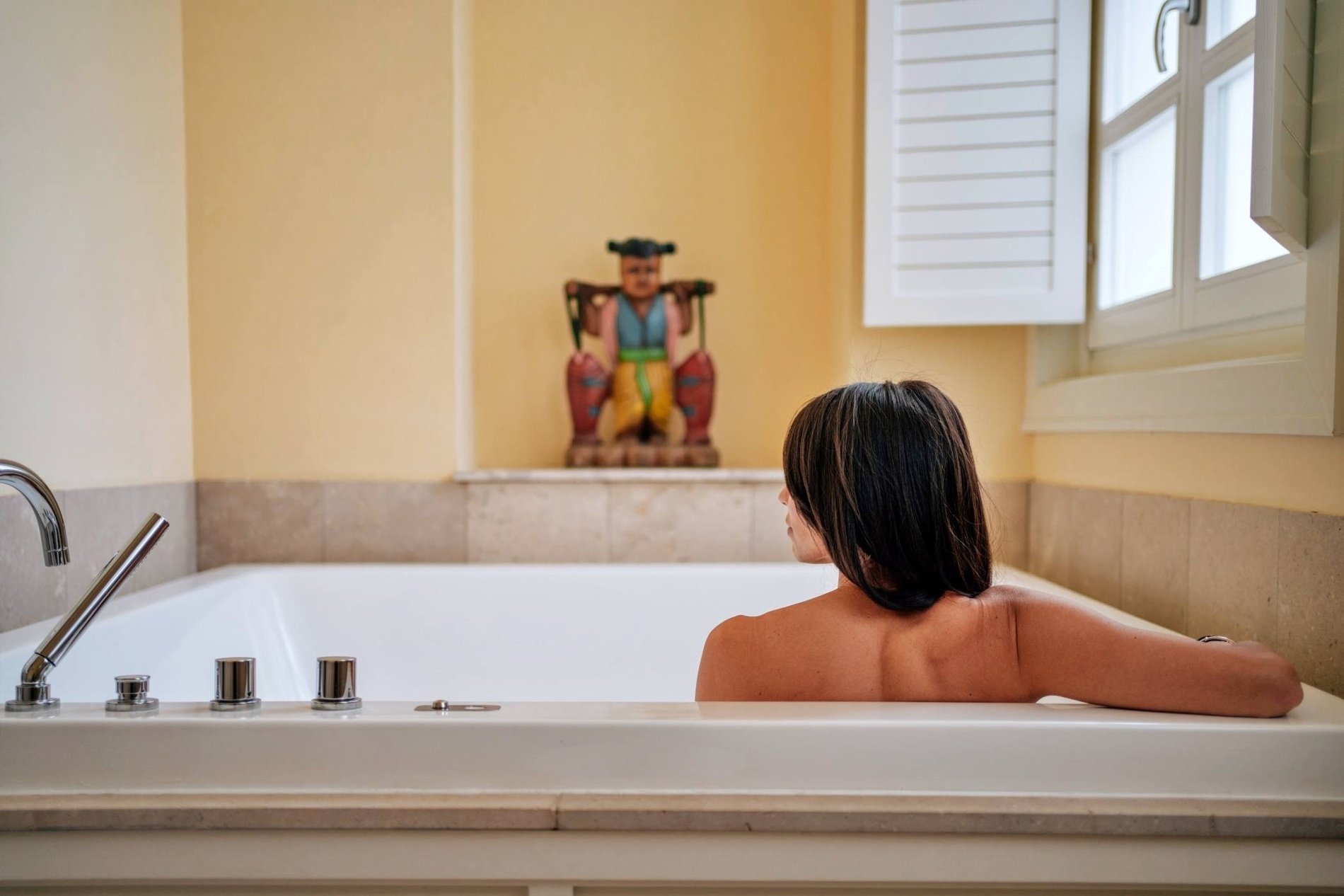 une femme se baigne dans une baignoire avec une statue en arrière-plan