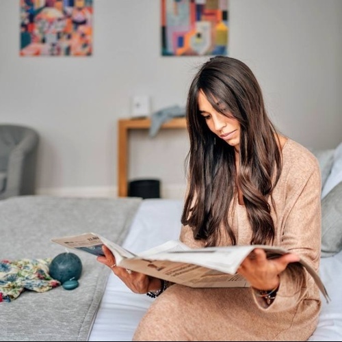 a woman sits on a bed reading a newspaper