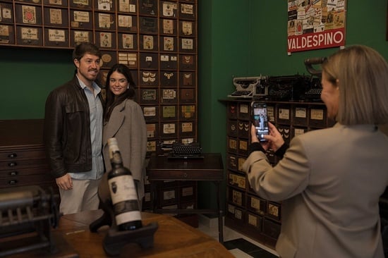 una mujer toma una foto de un hombre y una mujer en una habitación con un cartel de valdespino en la pared
