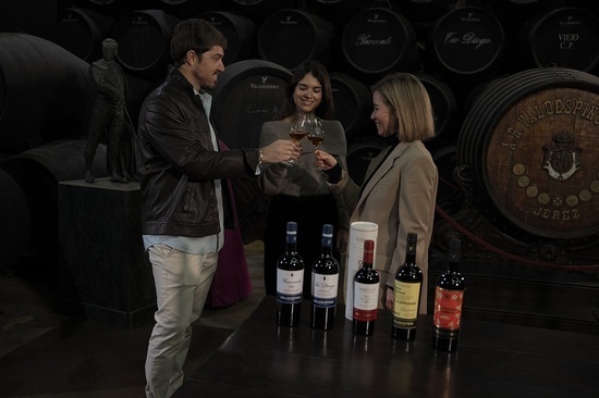 un hombre y dos mujeres brindan con botellas de vino