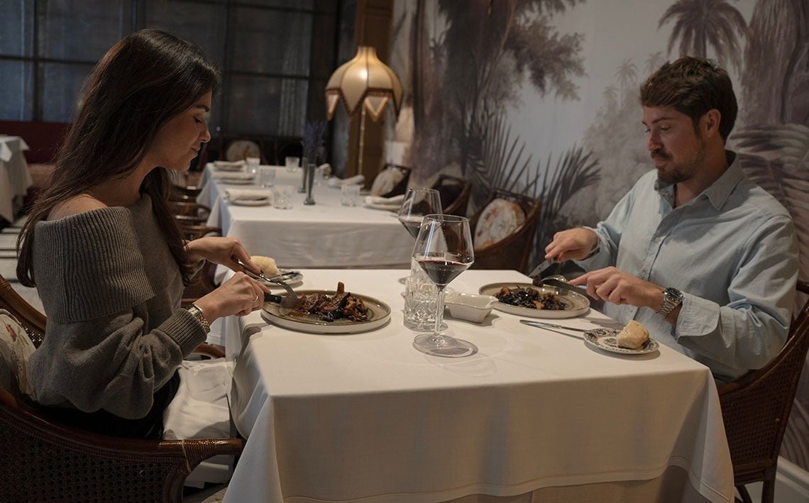 a man and a woman sit at a bar with bottles of macallan on the shelves