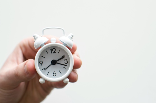 una persona sostiene un pequeño reloj de alarma blanco con las manos