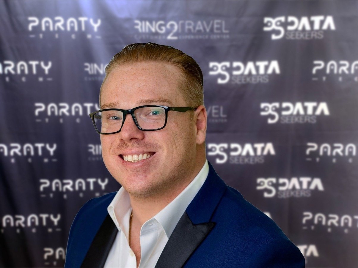 a man wearing glasses is smiling in front of a paraty banner