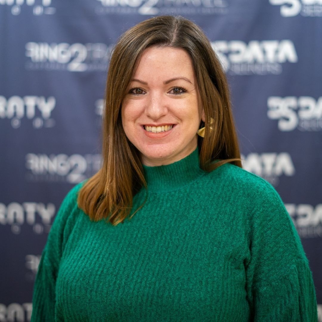 a woman in a green sweater smiles in front of a blue background that says data