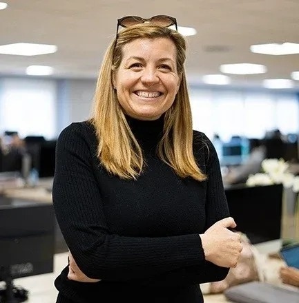 uma mulher com cabelo loiro e jaqueta preta sorri para a câmera