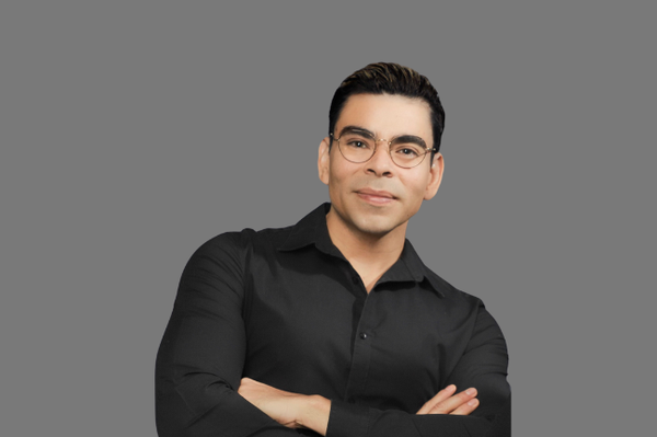 a man wearing glasses and a black shirt stands with his arms crossed