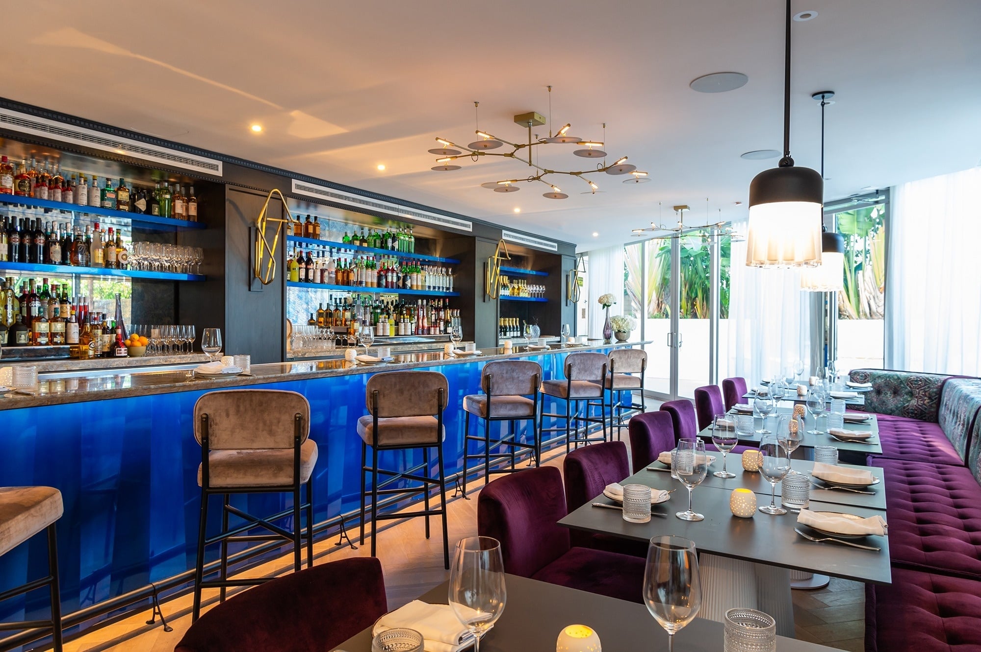 Chic hotel restaurant with plush pink chairs, botanical wallpaper, and warm wood tables.