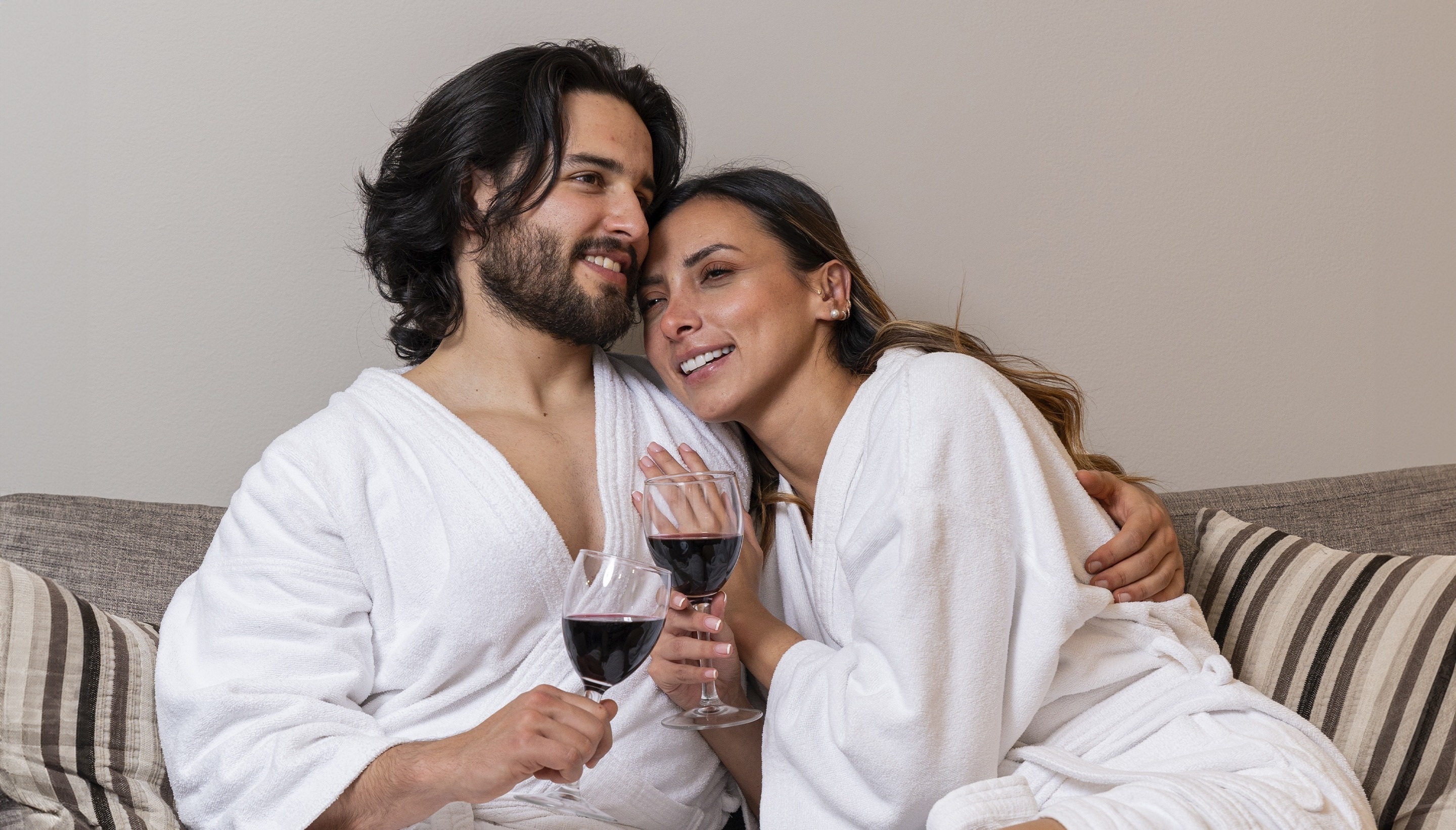 a man and a woman sitting on a couch holding wine glasses