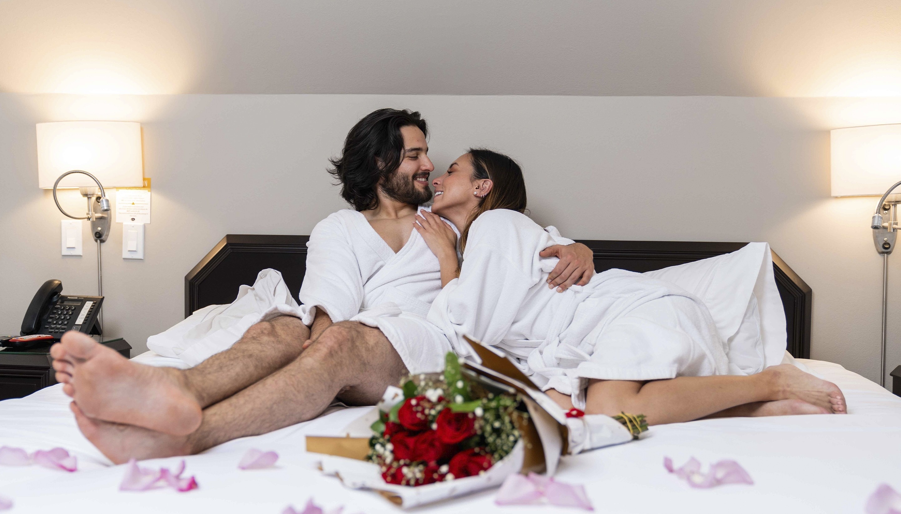 un hombre y una mujer están acostados en una cama con pétalos de rosa alrededor