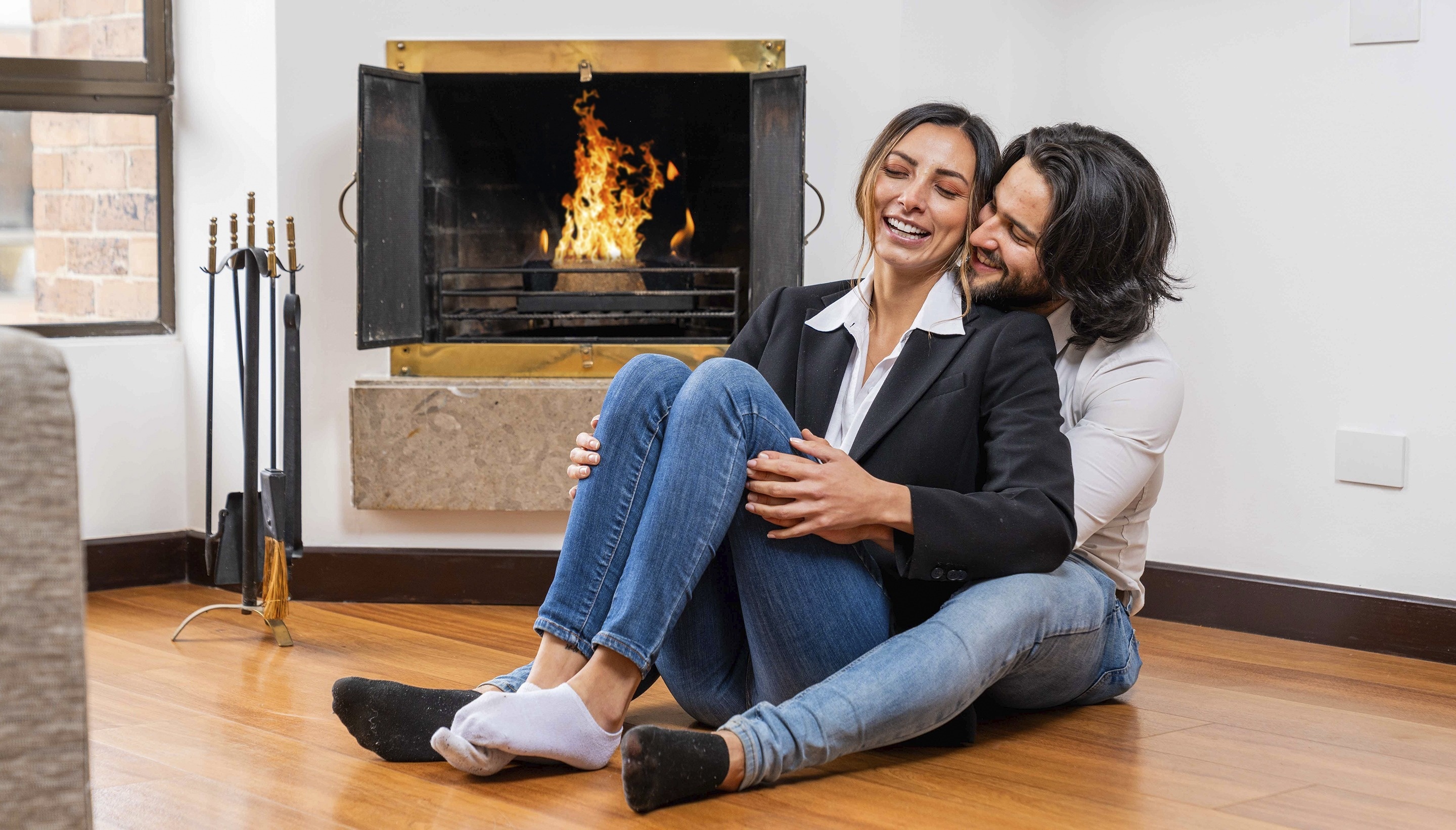 a man and woman sit on the floor in front of a fireplace