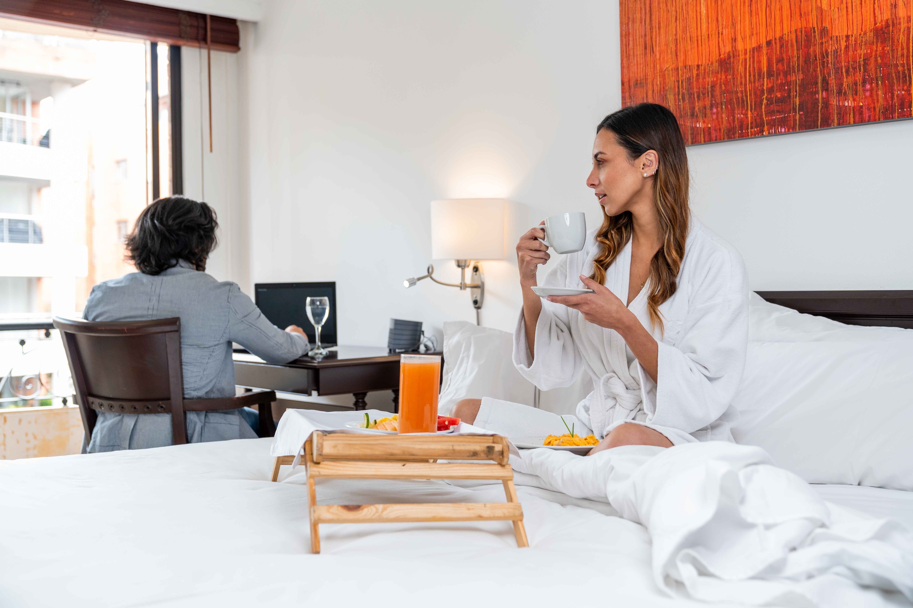 una mujer está sentada en una cama con una bandeja de comida y una taza de café