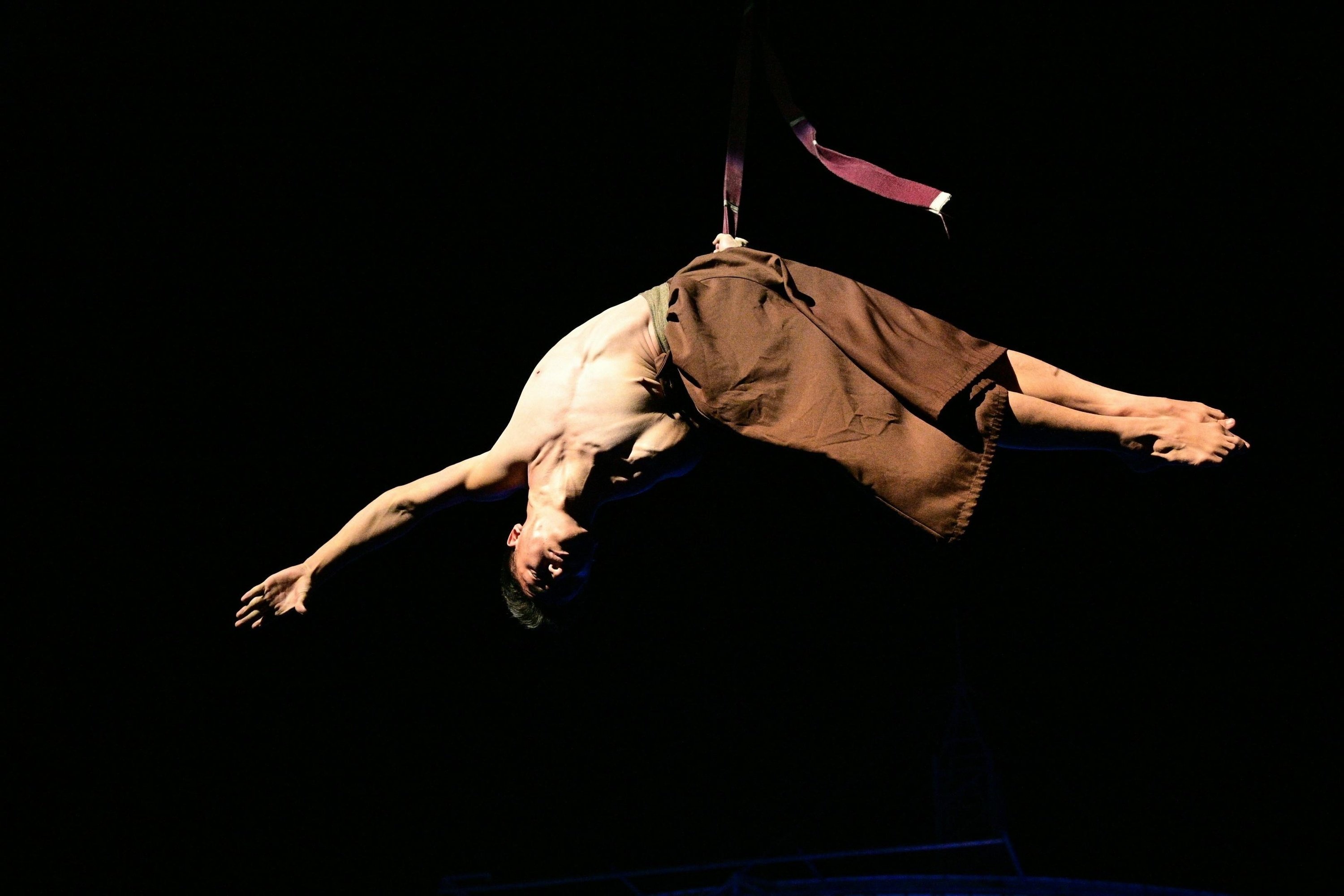 um homem sem camisa está pendurado no ar com uma fita vermelha