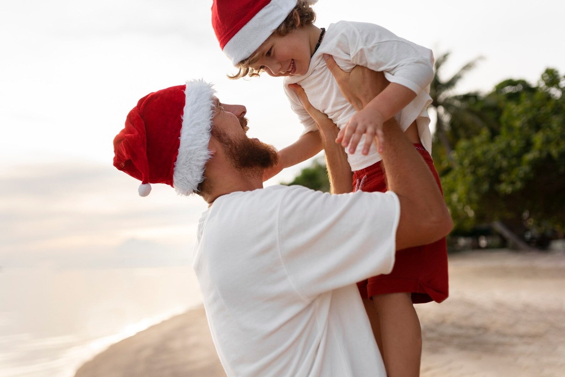 un hombre sostiene a un niño con un sombrero de santa en la playa