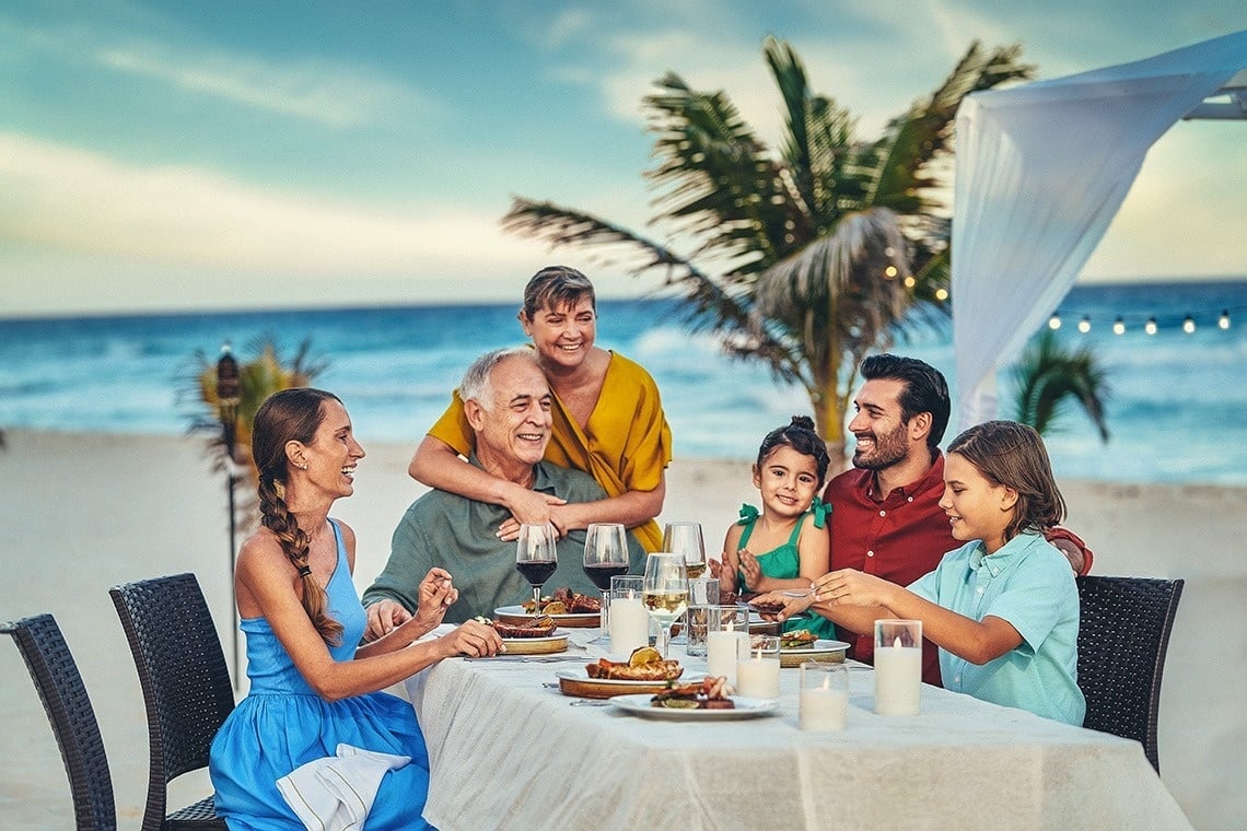 una familia se sienta en una mesa en la playa comiendo