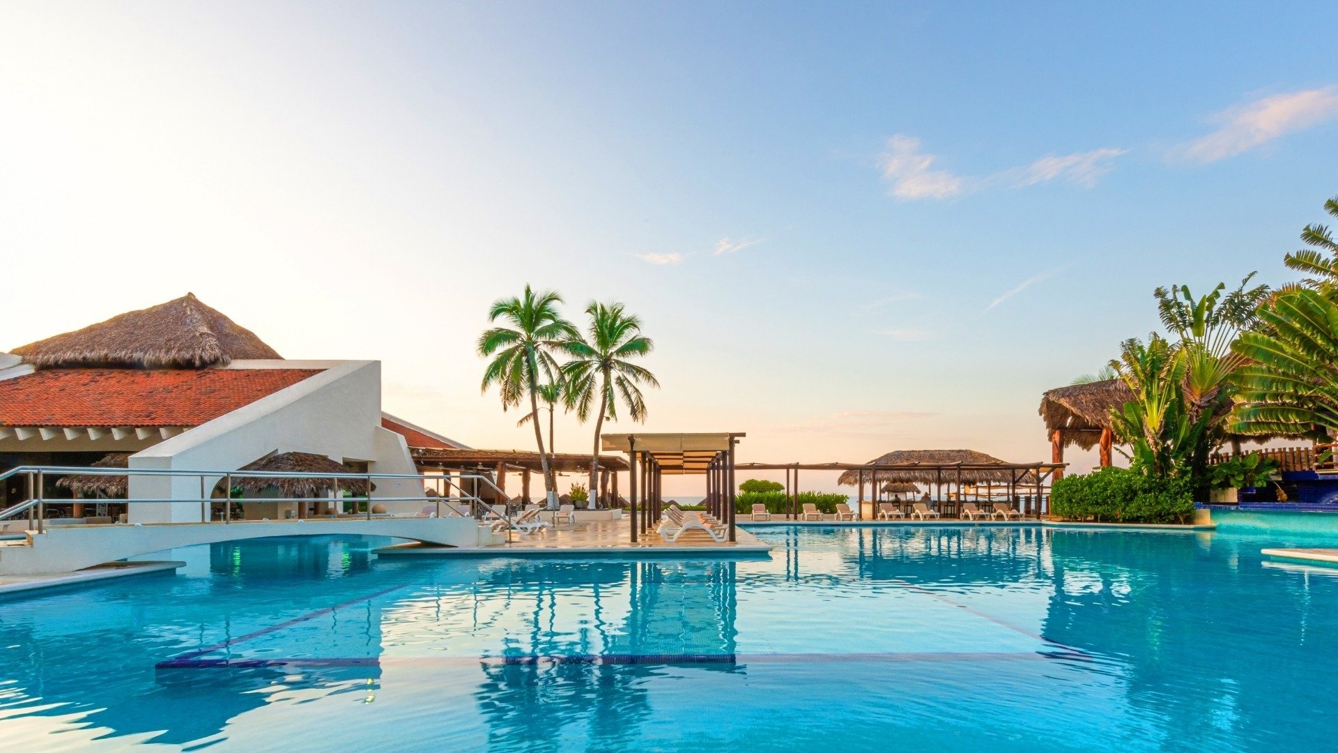 a large swimming pool surrounded by thatched huts and palm trees