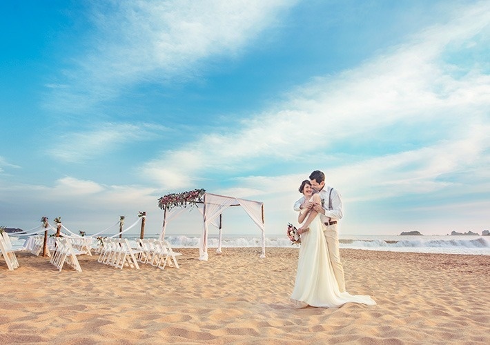 a bride and groom standing on a sandy beach