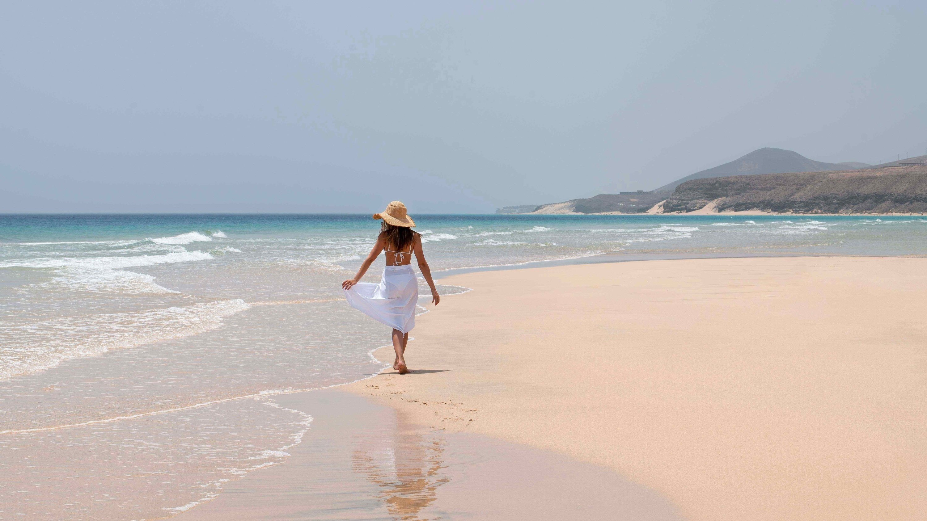 una mujer con un sombrero camina por la playa