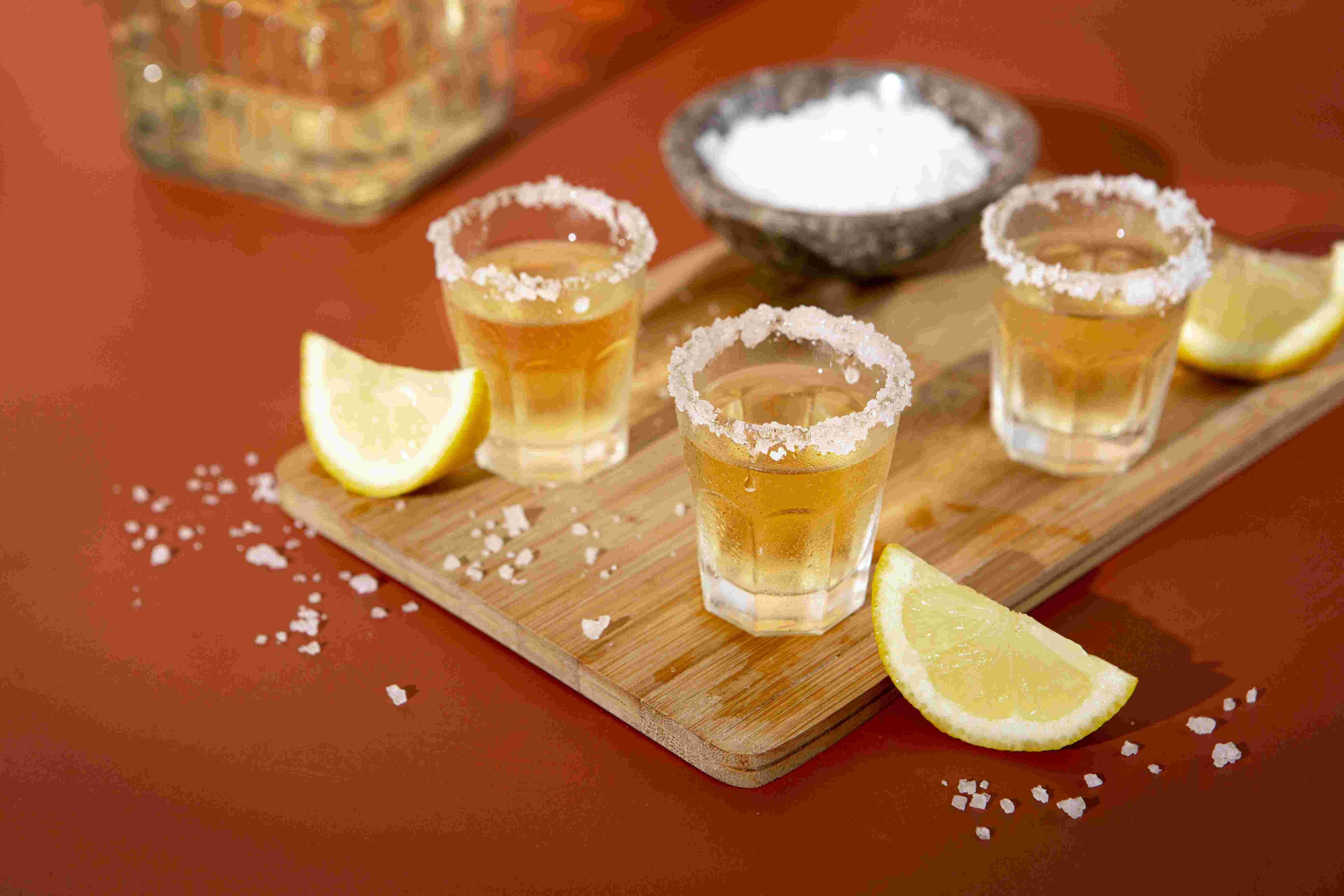 três copos de tequila com limão e sal em uma tábua de madeira