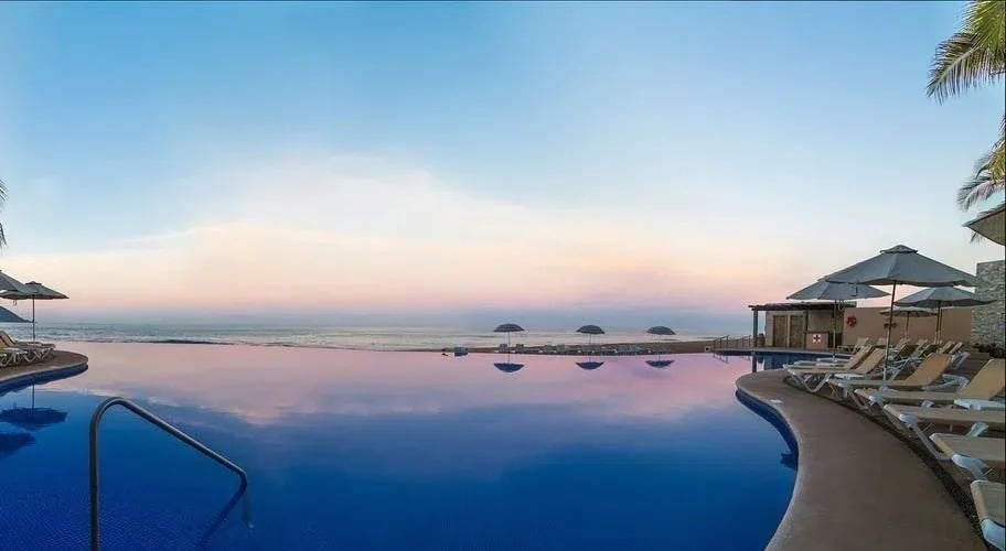 a large swimming pool surrounded by chairs and umbrellas overlooking the ocean .