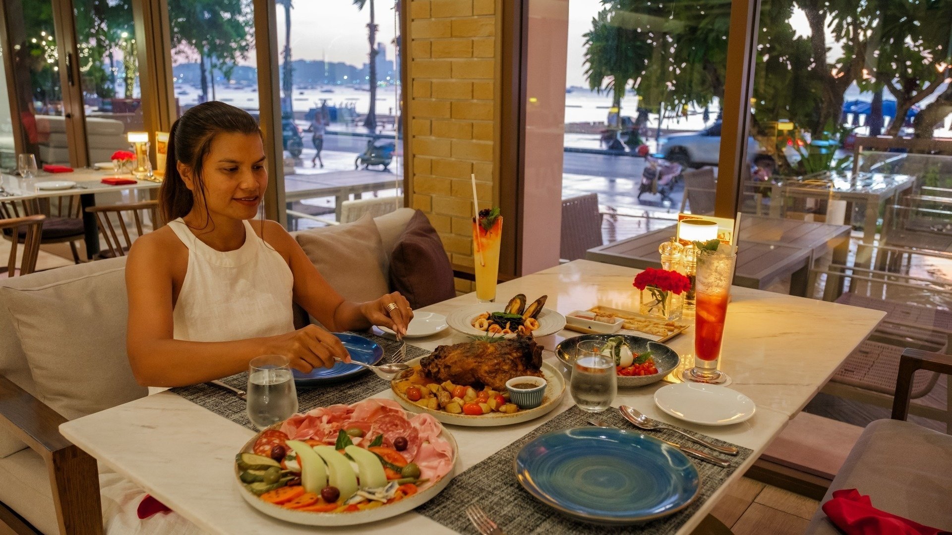 una mujer se sienta en una mesa con platos de comida y bebidas