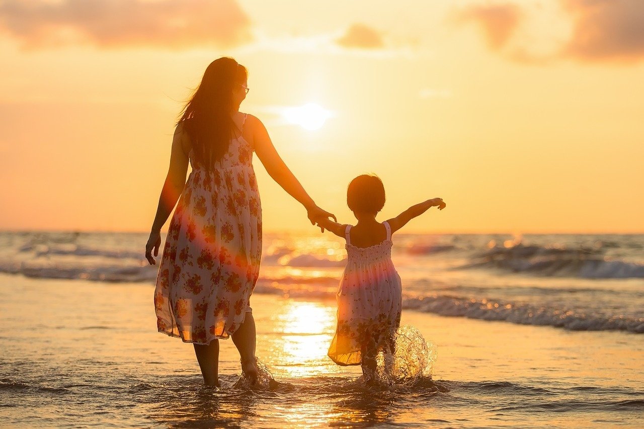a woman and child are walking on the beach at sunset