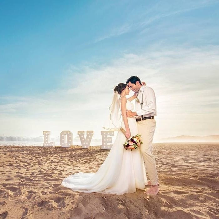 Newlyweds on the beach, next to them there are letters with lights that form the word love, from the Hotel Park Royal Beach Huatulco