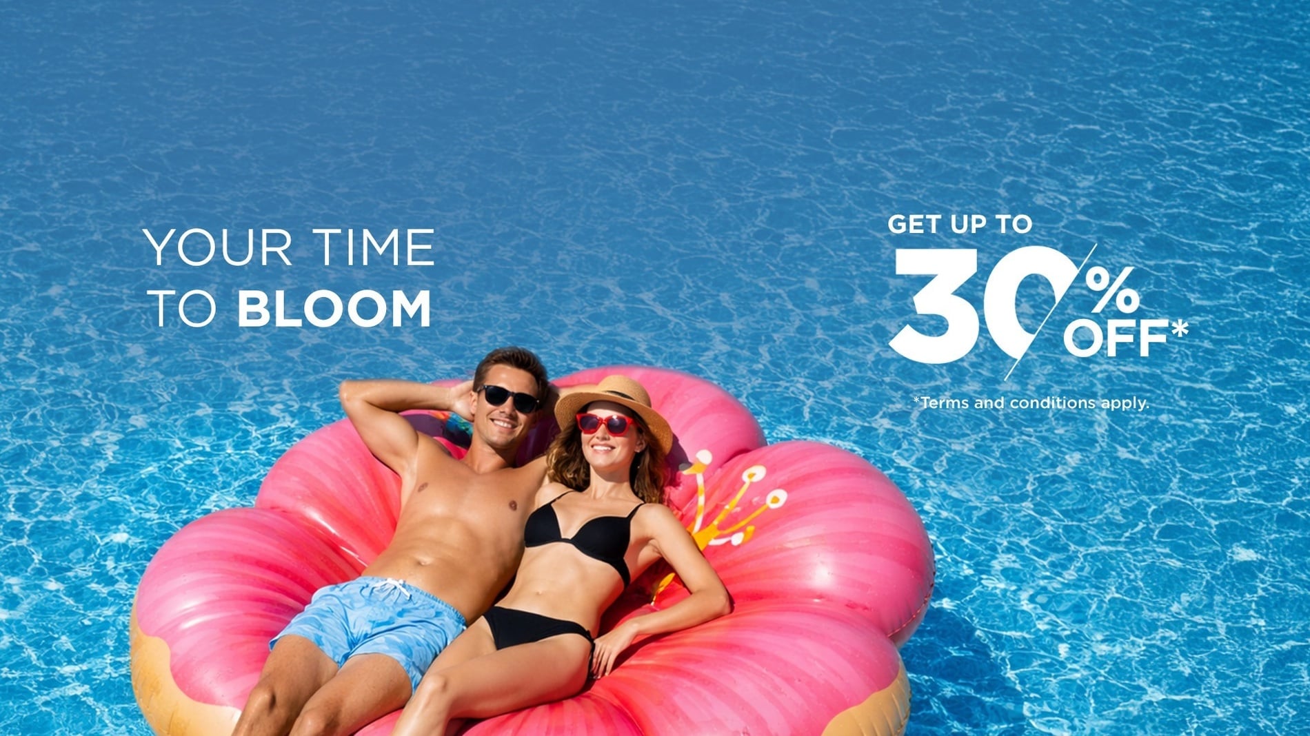 A couple relaxes on a pink flower-shaped inflatable in a swimming pool, alongside promotional text offering "YOUR TIME TO BLOOM" with "GET UP TO 30% OFF*" and "+ FREE SHUTTLE".