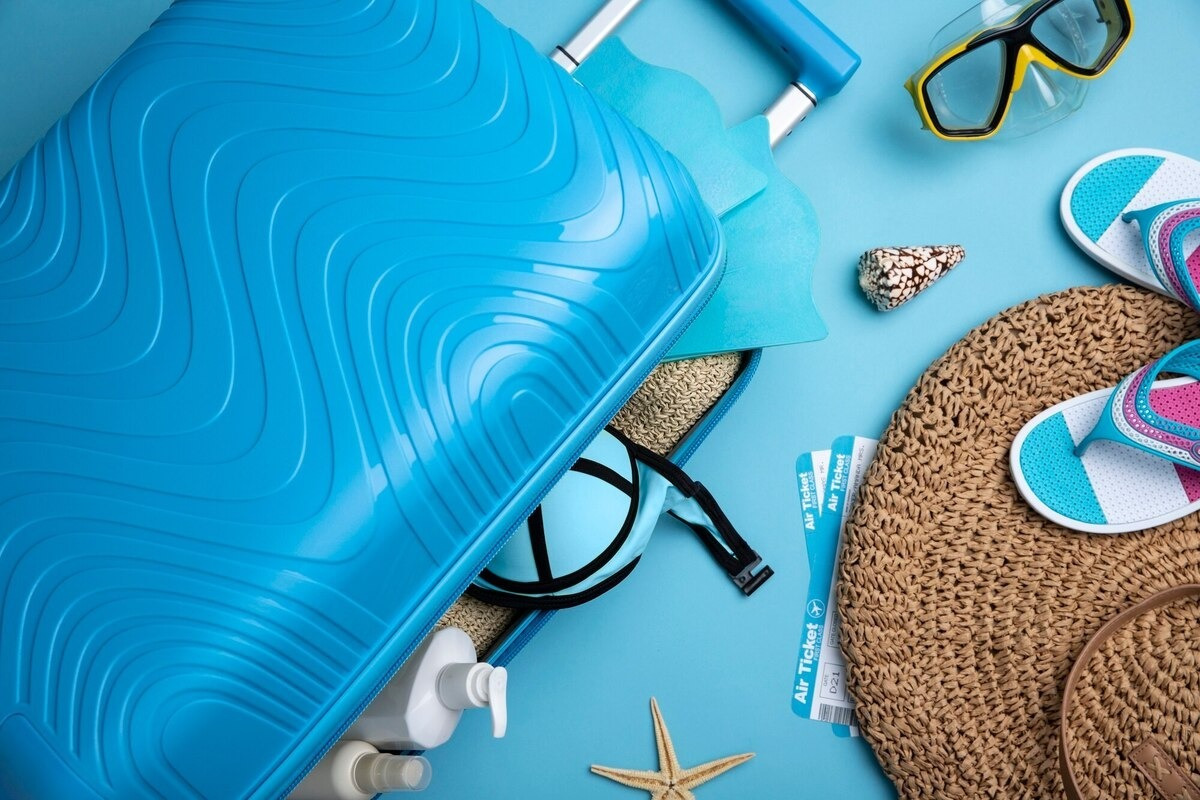 Maleta azul abierta con artículos de playa, boletos aéreos y Park Royal