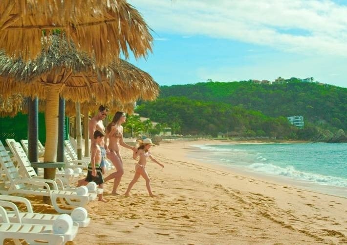 a family walking on a beach under thatched umbrellas