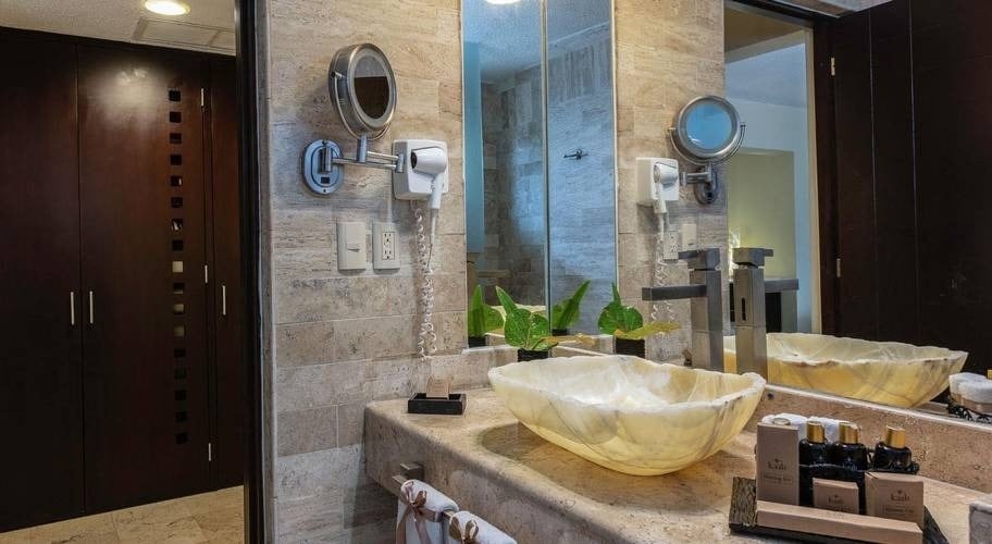 Lavatório com um conjunto de produtos de banho, secador de cabelo e espelho no Grand Park Royal Cancun Hotel