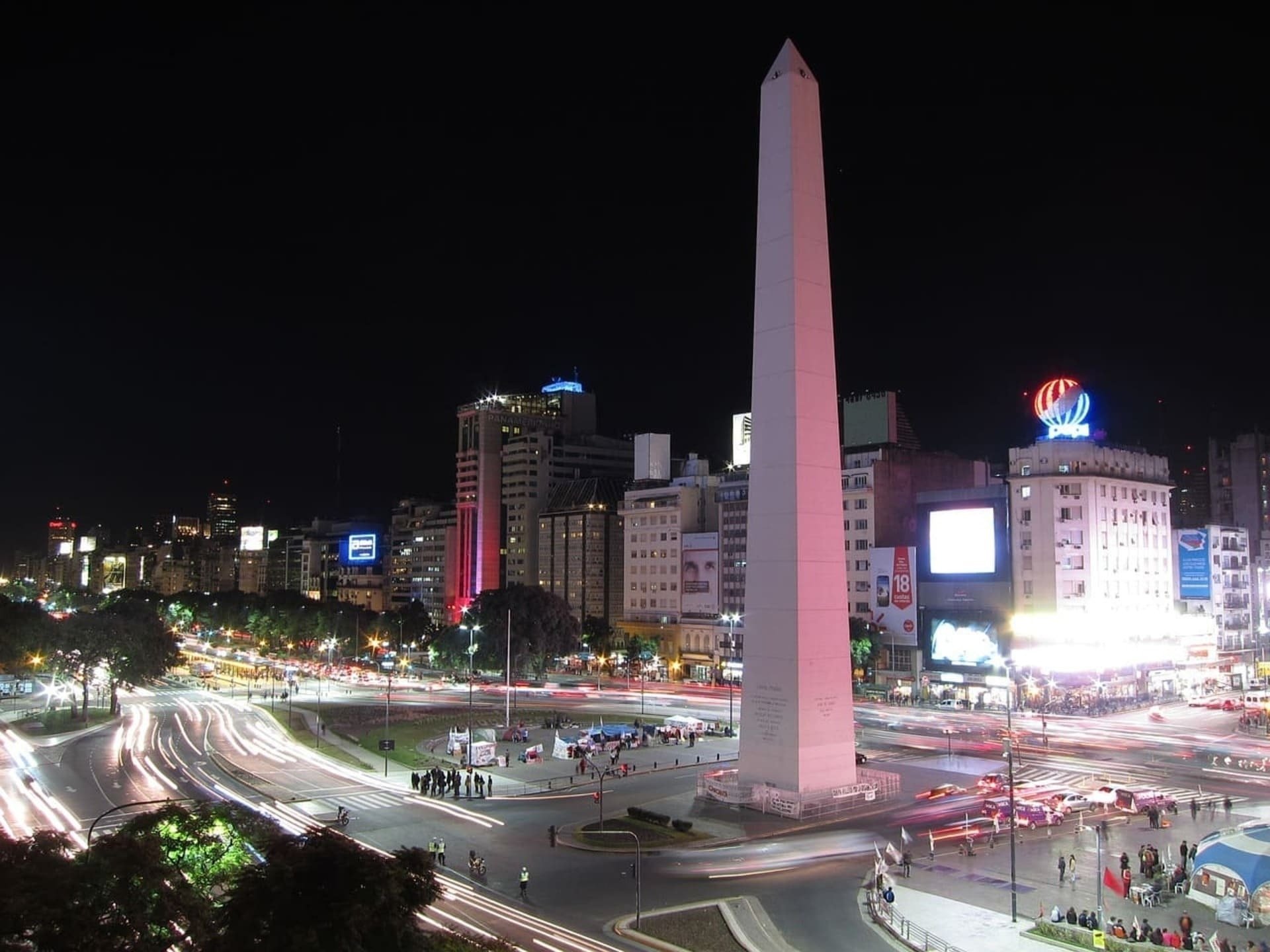 uma cidade à noite com um obelisco em primeiro plano