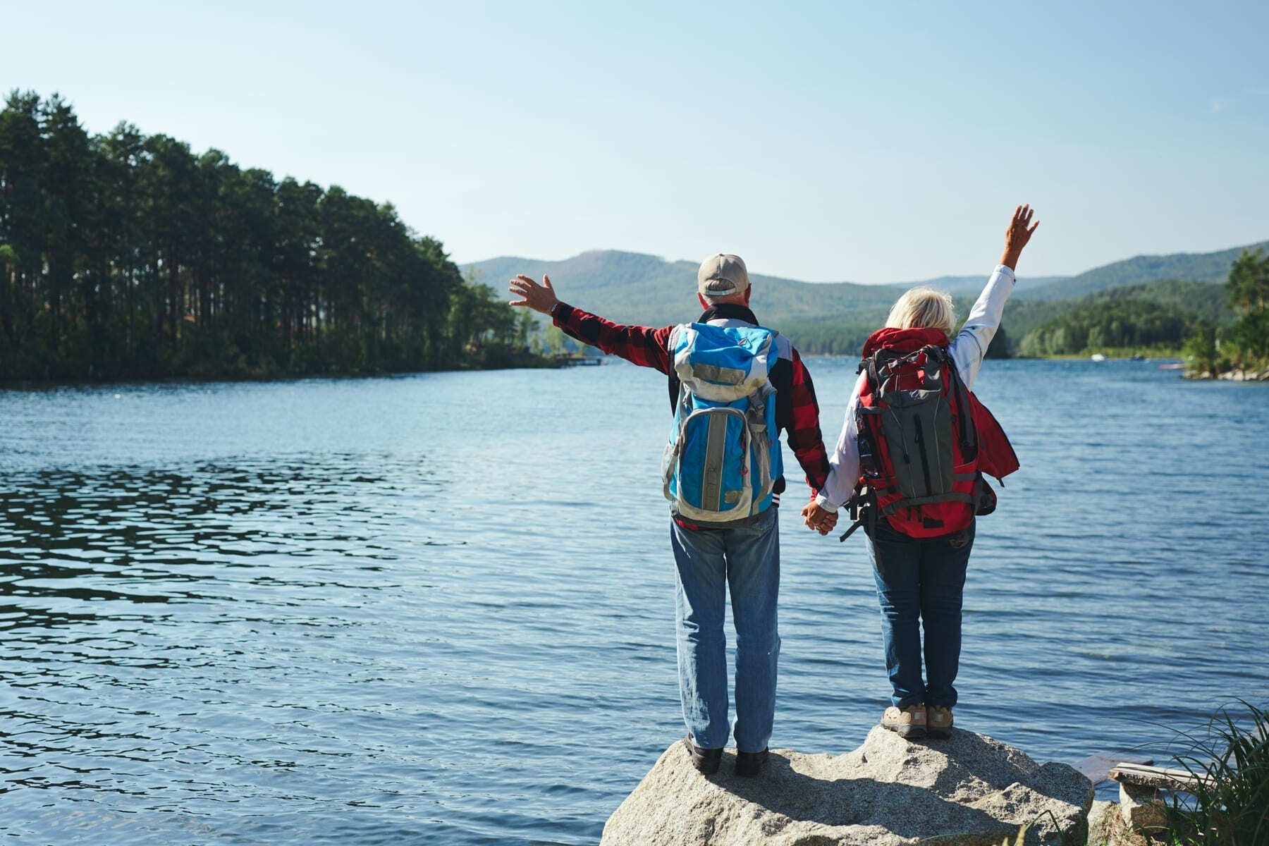 un hombre y una mujer con mochilas se paran en una roca junto a un lago