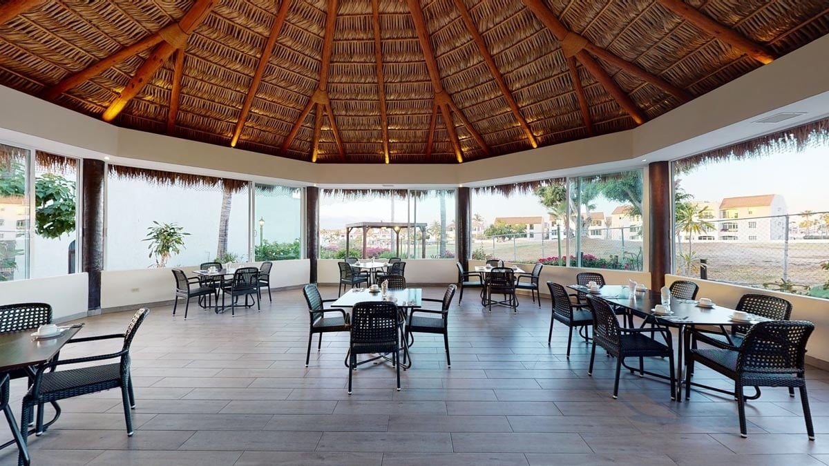 a large room with tables and chairs under a thatched roof