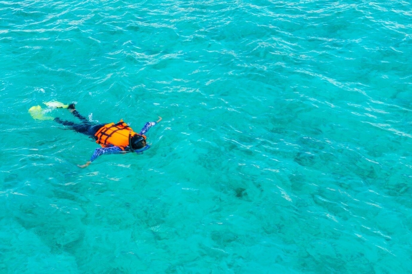 uma pessoa está flutuando no oceano usando um colete salva-vidas laranja