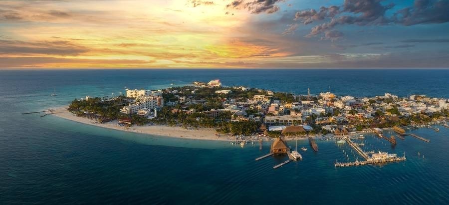 uma vista aérea de uma pequena ilha no oceano ao pôr do sol .