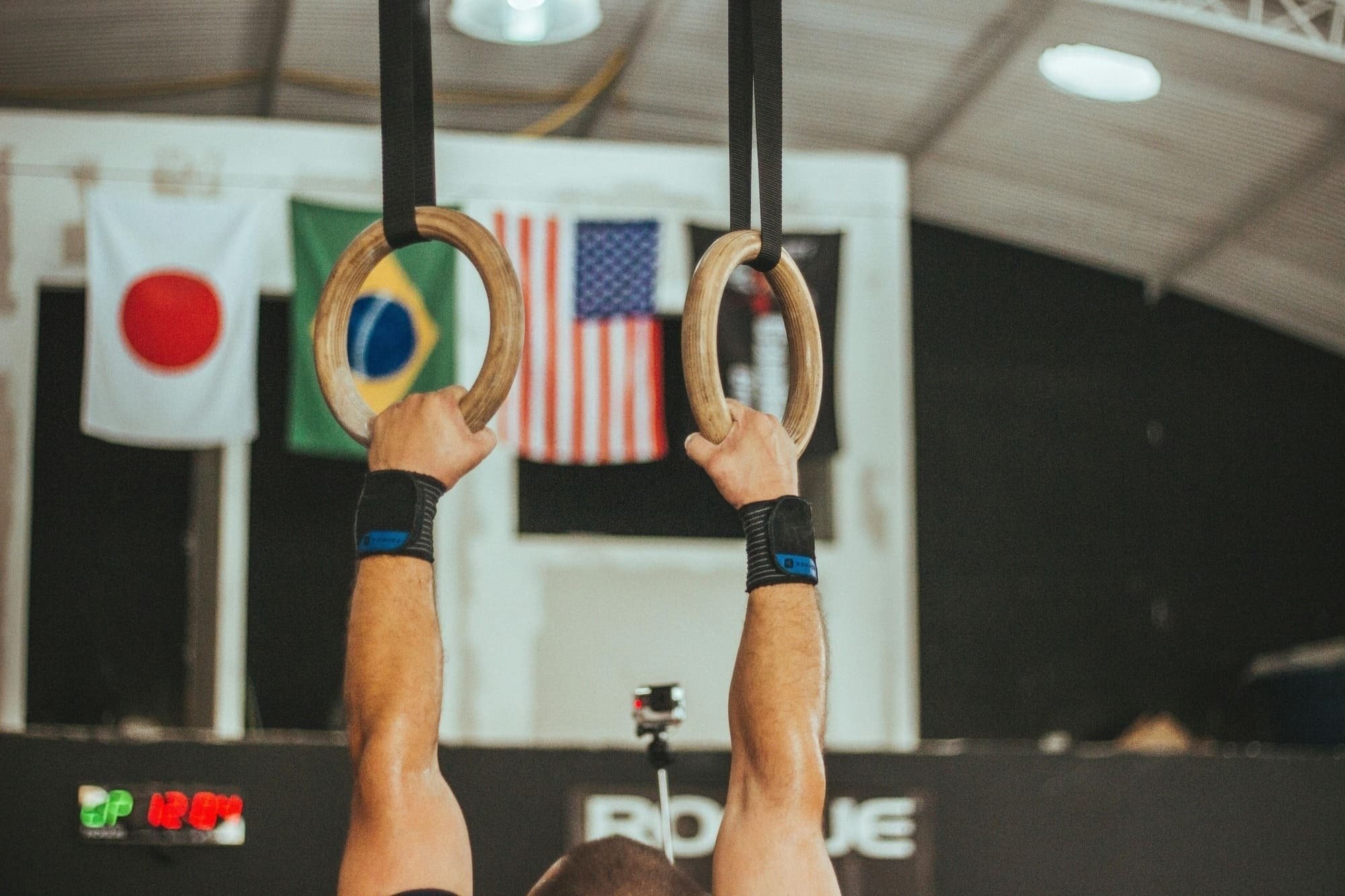 un hombre sostiene anillos de gimnasia en un gimnasio con banderas en el fondo